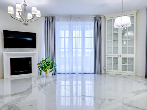Bright modern living room with marble floor, fireplace, wall-mounted TV, chandelier, and large window with sheer curtains.